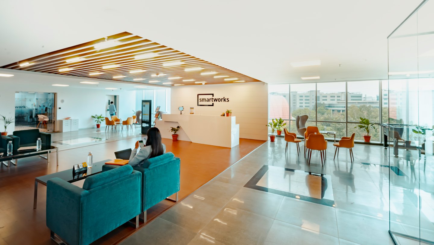 Donna su divano verde acqua usa il telefono in una reception moderna.